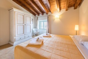 A bedroom with a large bed, a wardrobe, a chair, and a window with curtains.