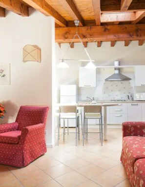 A room with a wooden ceiling, a dining area with chairs and a table, and a bed with a floral pattern. - Apartment 'Antica Torre Goethe' with Mountain View, Wi-Fi and Air Conditioning (San Felice del Benaco (BS))