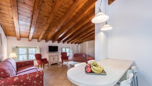 Un vaste espace de vie doté d’un plafond en bois, d’une table à manger ornée de fruits, d’un canapé et de deux fauteuils.