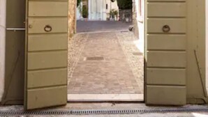 On aperçoit, à travers un grand portail ouvert, une rue étroite bordée de bâtiments des deux côtés.
