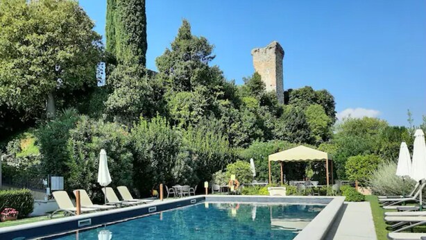 A rectangular swimming pool with lounge chairs and umbrellas, surrounded by lush greenery and a historic tower in the background. - Apartment 'Antica Torre D Annunzio' with Mountain View, Wi-Fi and Air Conditioning (San Felice del Benaco (BS))