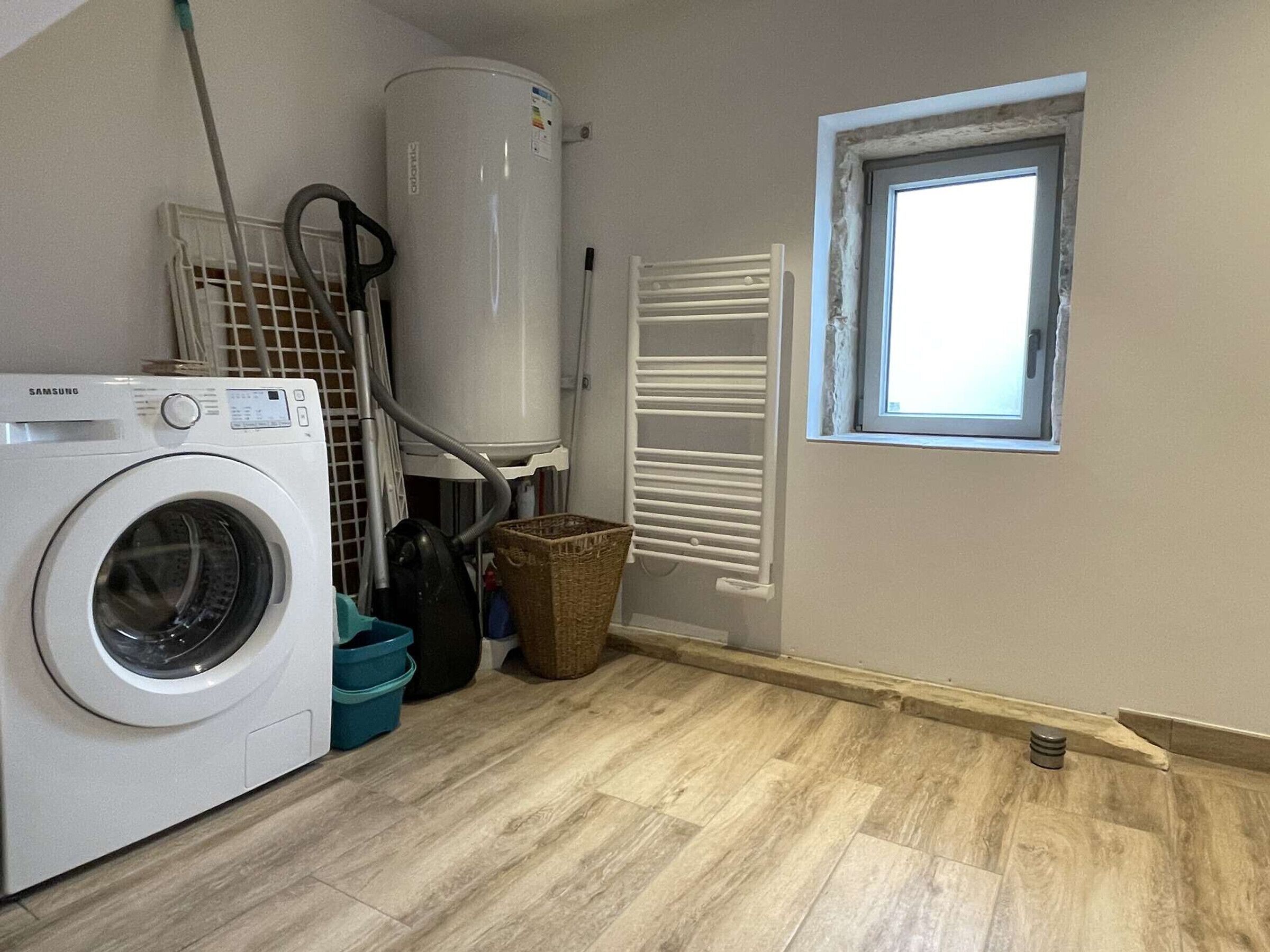 A laundry room with a washing machine, a water heater, a window, and a radiator.