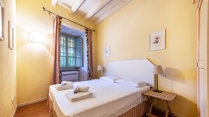 Una habitación de hotel con una cama, una mesita de noche con lámpara, una ventana con cortinas y un cuadro en la pared.