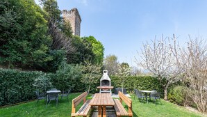 Una mesa de picnic con bancos, una parrilla y una torre de piedra al fondo.
