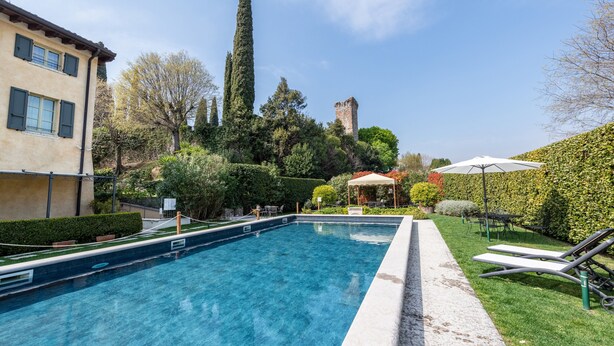 Una piscina con sillones de descanso, un pabellón y un castillo al fondo.