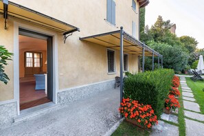 Un edificio con un'area esterna coperta, un vialetto in pietra e fiori rossi.