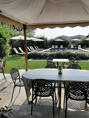 Een terras buiten met een tafel en stoelen, omringd door planten en parasols.