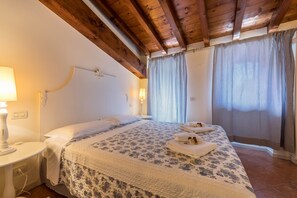 Een slaapkamer met een houten plafond, een bed met een bloemenprint sprei, een nachtkastje met een lamp en gordijnen.