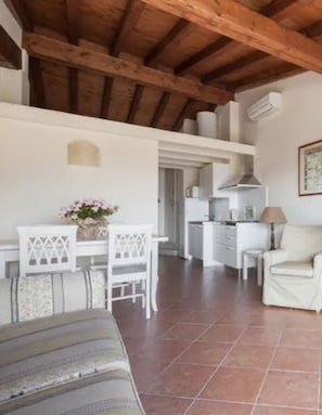 Une pièce avec un plafond en bois, des meubles blancs, un coin cuisine et un sol carrelé.