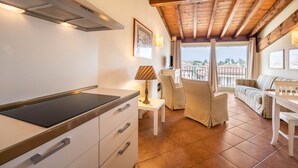 A modern kitchen with a built-in stove, a dining area with a sofa and table, and a balcony with a view. - Apartment 'Antica Torre Byron' with Shared Pool, Wi-Fi and Air Conditioning (San Felice del Benaco (BS))