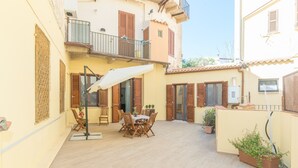 A courtyard with a table and chairs, a white umbrella, and potted plants. - Apartment 'Rifla Vacanze' with Terrace & Wi-Fi (La Maddalena)