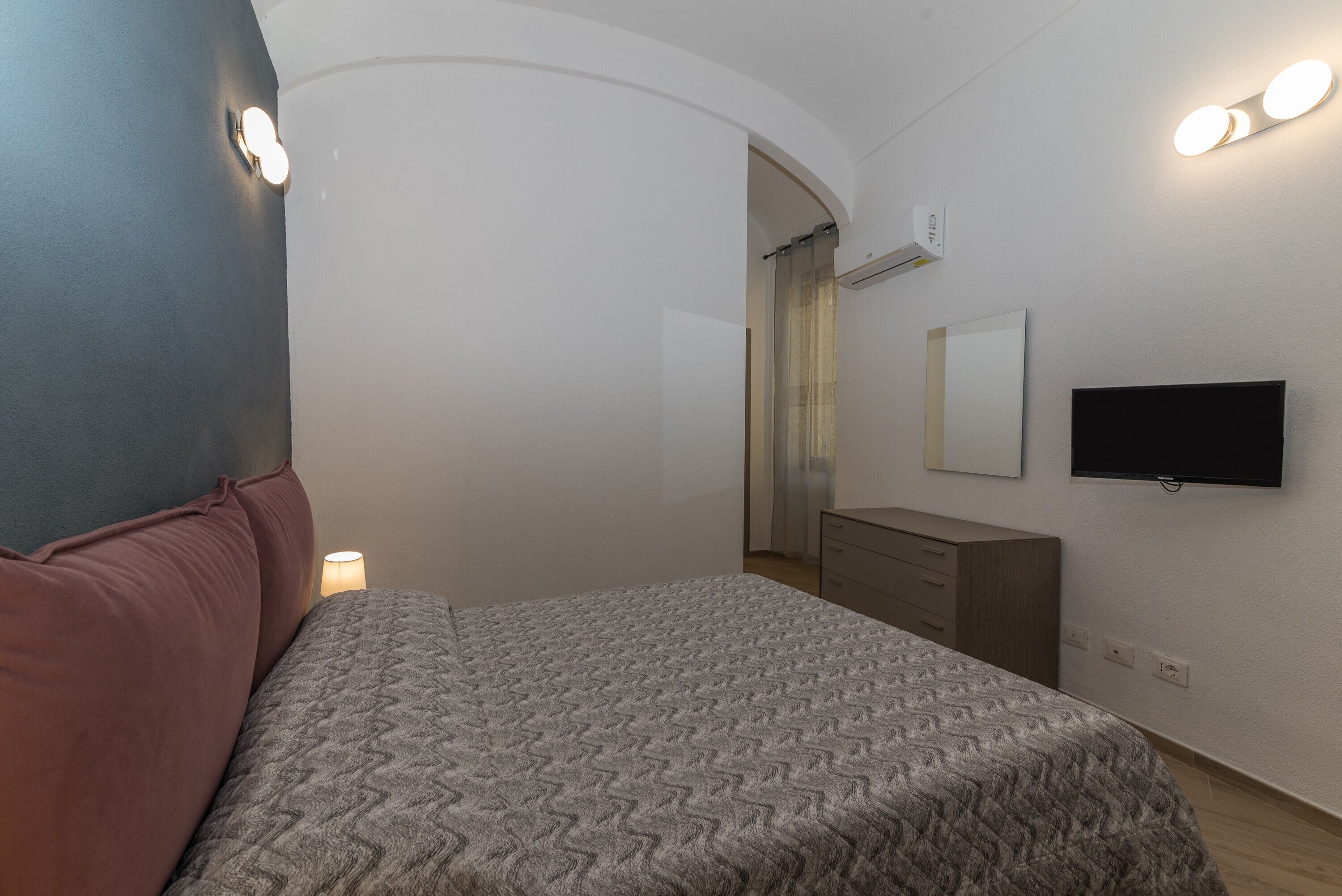 Ein Schlafzimmer mit Bett, Kommode, Fernseher und Spiegel.