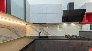 A modern kitchen with a marble backsplash, dark cabinetry, and a built-in stove. - Apartment 'Rifla Vacanze' with Terrace & Wi-Fi (La Maddalena)