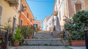 A cobblestone street leading up to a set of stone steps, flanked by buildings with balconies and potted plants. - Apartment 'Rifla Vacanze' with Terrace & Wi-Fi (La Maddalena)