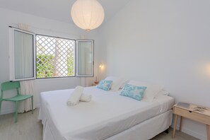 A bedroom with a bed, a chair, a bedside table, and a window with a view.