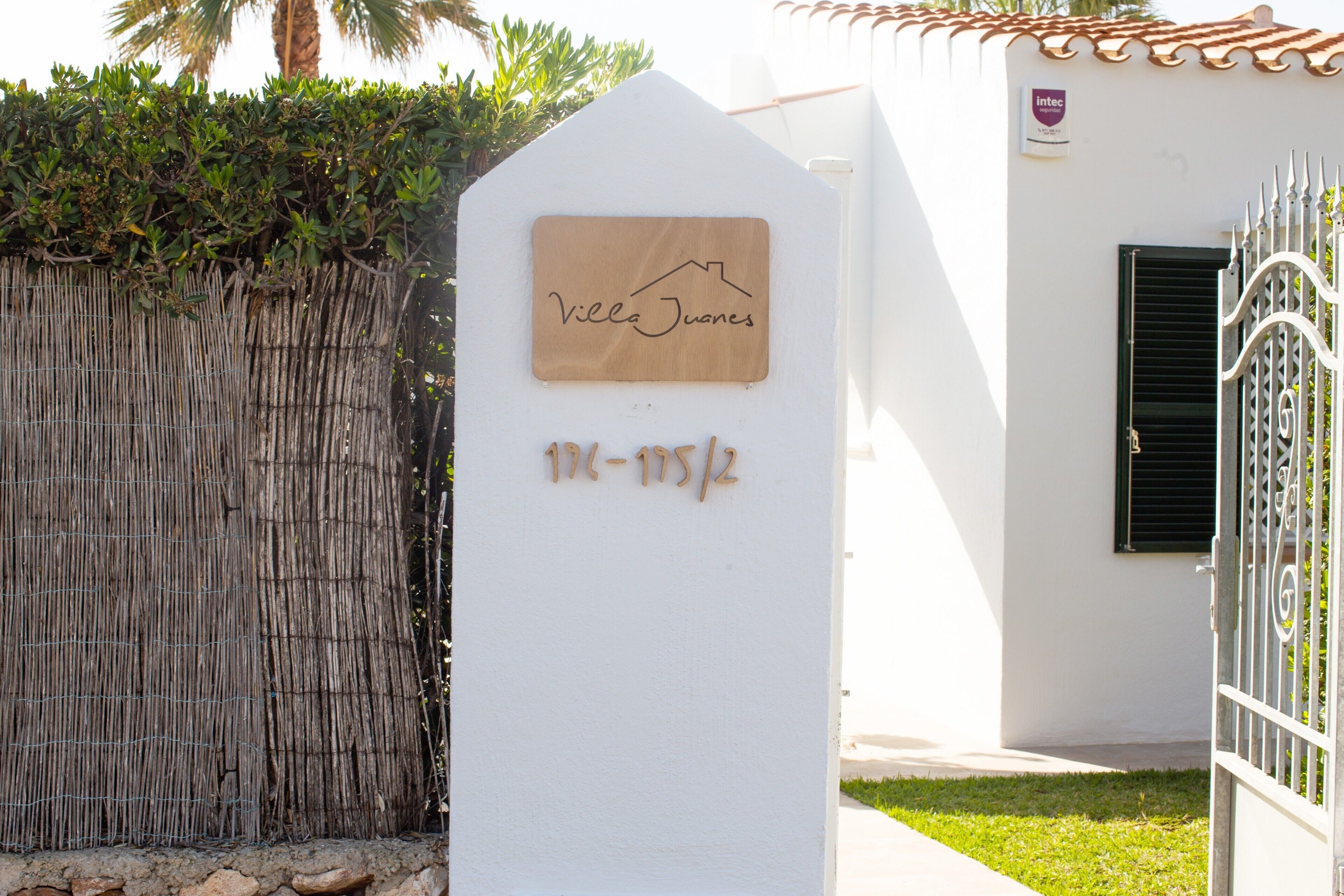 Un edificio blanco con una placa de madera que dice 'Villa Juanes' y el número '176-175/2'.