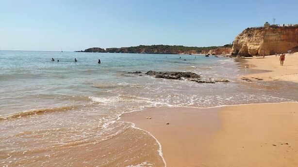 A beach with clear water, a sandy shore, and rocky cliffs in the background.