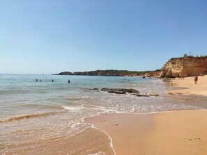 Una spiaggia con acque limpide, una riva sabbiosa e scogliere rocciose sullo sfondo.