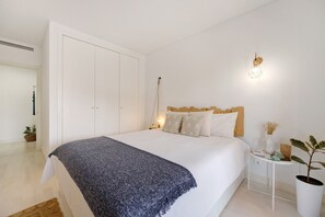 Un dormitorio con cama, mesita de noche, lámpara y una planta en maceta.