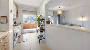 A modern kitchen with a washing machine, a drying rack, and a small shelf with plants.