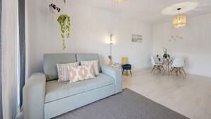 A modern living room with a sofa, a dining table with chairs, and hanging plants.
