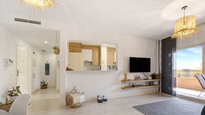 A modern living room with a flat-screen TV, a large mirror, and a dining area with chairs and a table.