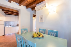 A dining area with a table set for four, a fruit tray, and a kitchen in the background.