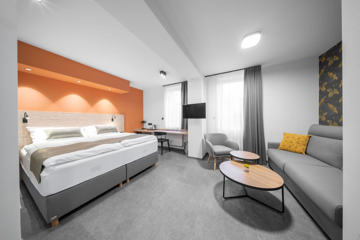A modern hotel room with a bed, a sofa, a desk, and a TV.