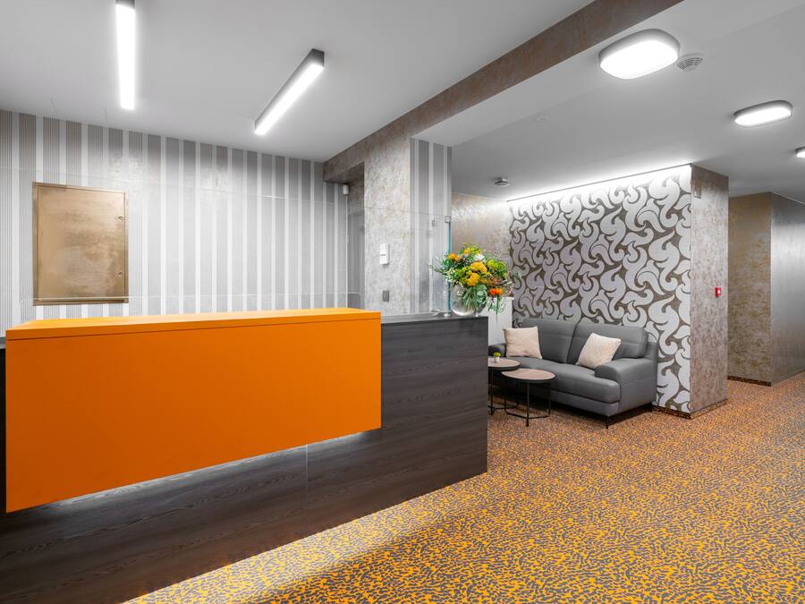 A reception area with a modern design, featuring a wooden reception desk, a grey sofa, and a patterned wall.