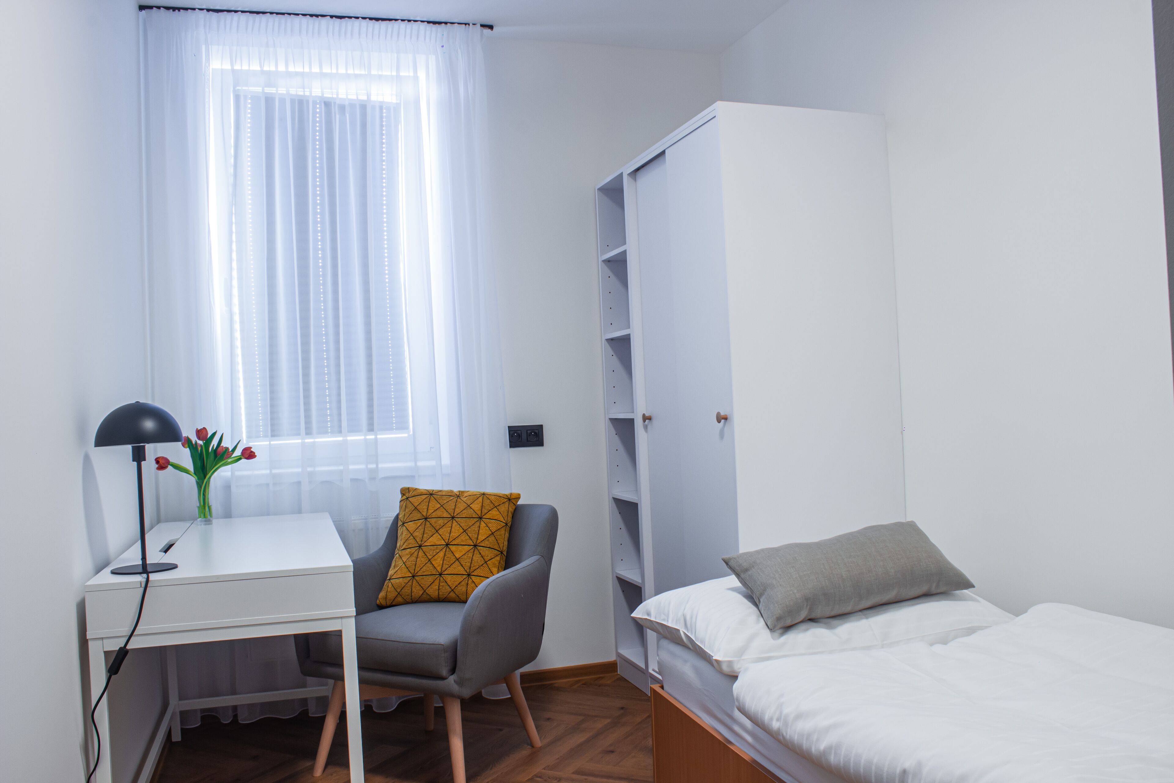 Un dormitori amb un llit, un escriptori amb una cadira, un armari i una finestra amb cortines.