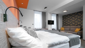 Una habitación de hotel moderna con una cama grande, un sofá, un televisor de pantalla plana y un escritorio.