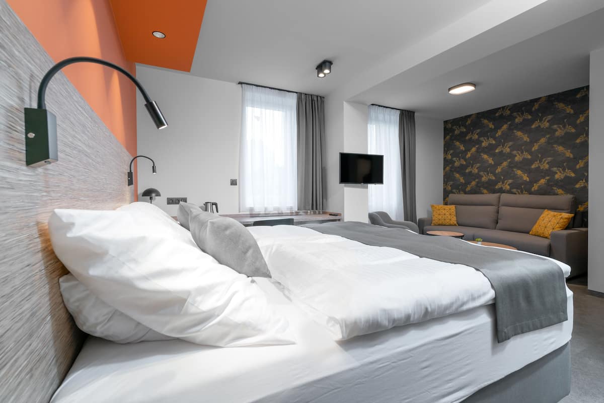 A modern hotel room with a large bed, a sofa, a flat-screen TV, and a desk.