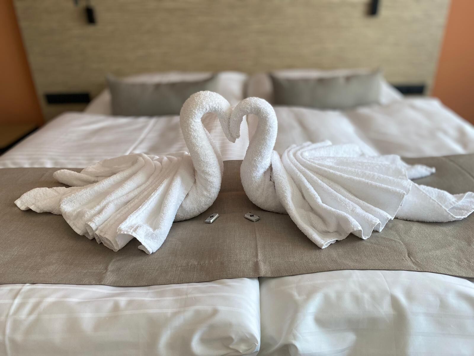 A bed with white linens and two towels arranged in the shape of swans.