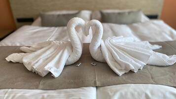 A bed with white linens and two towels arranged in the shape of swans.