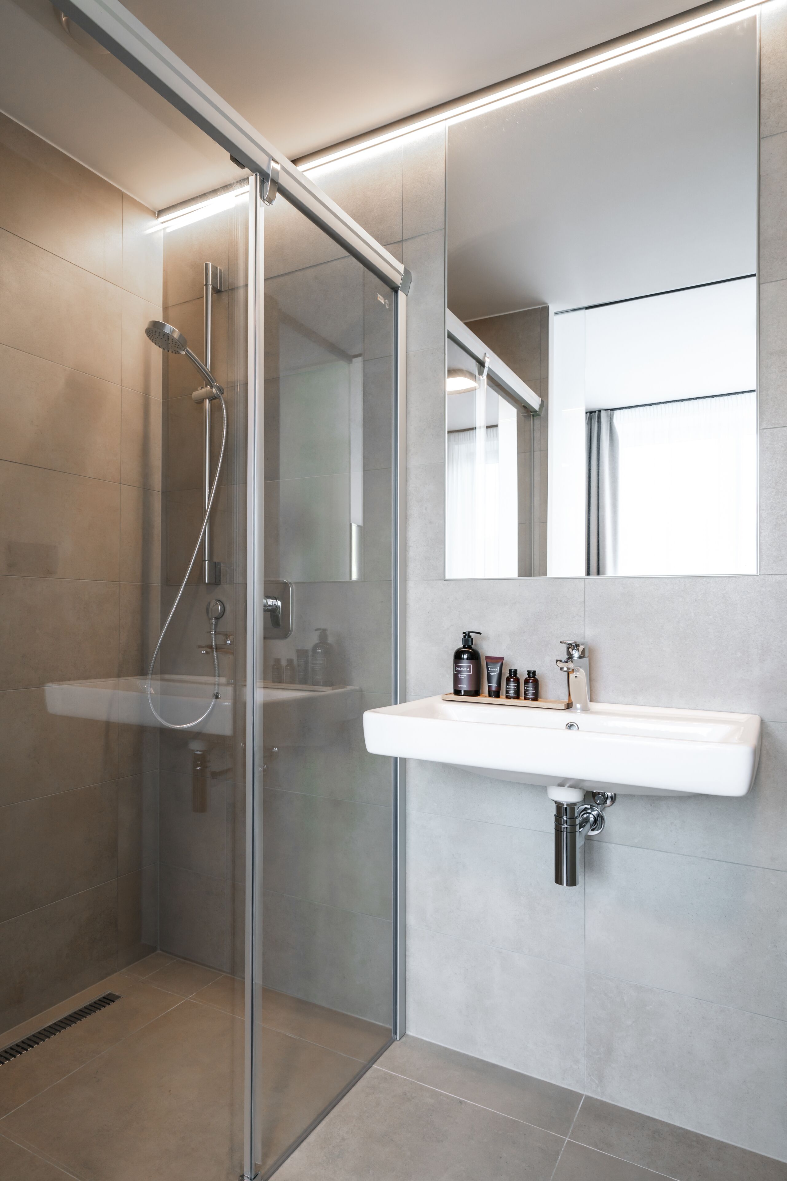A modern bathroom with a glass-enclosed shower, a white sink, and a mirror above it.