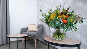 Una habitación moderna con un sofá gris, dos mesas redondas y un gran arreglo floral sobre una de ellas.