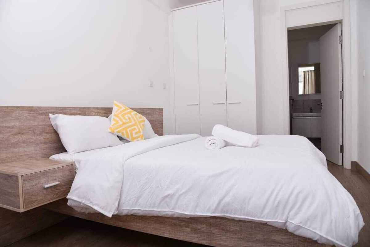 Ein ordentlich bezogenes Bett mit weißer Bettwäsche und einem Holzkopfende, ein kleiner Nachttisch und ein Schrank mit weißen Türen.