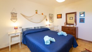 Een slaapkamer met een bed, nachtkastjes, een dressoir, een hangend net, wanddecoratie en een lamp.
