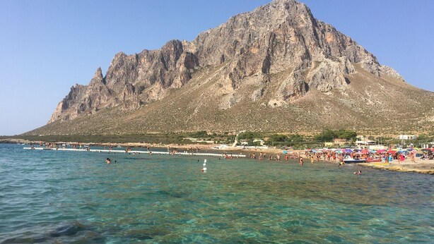 Een bergachtig landschap met helder water en een strand vol mensen.