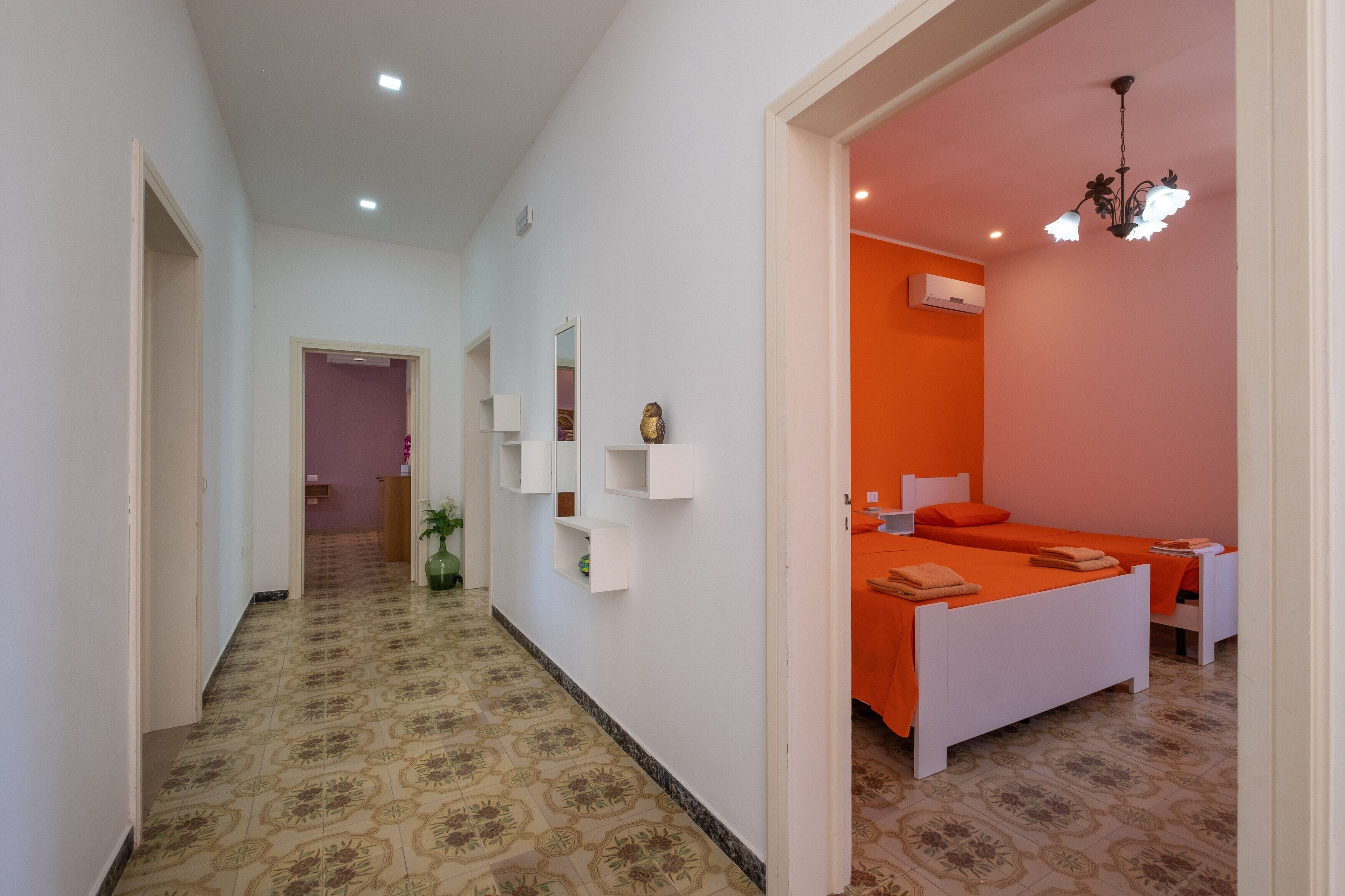 A hotel room with a hallway leading to a bedroom, a small plant, and a decorative ceiling light.