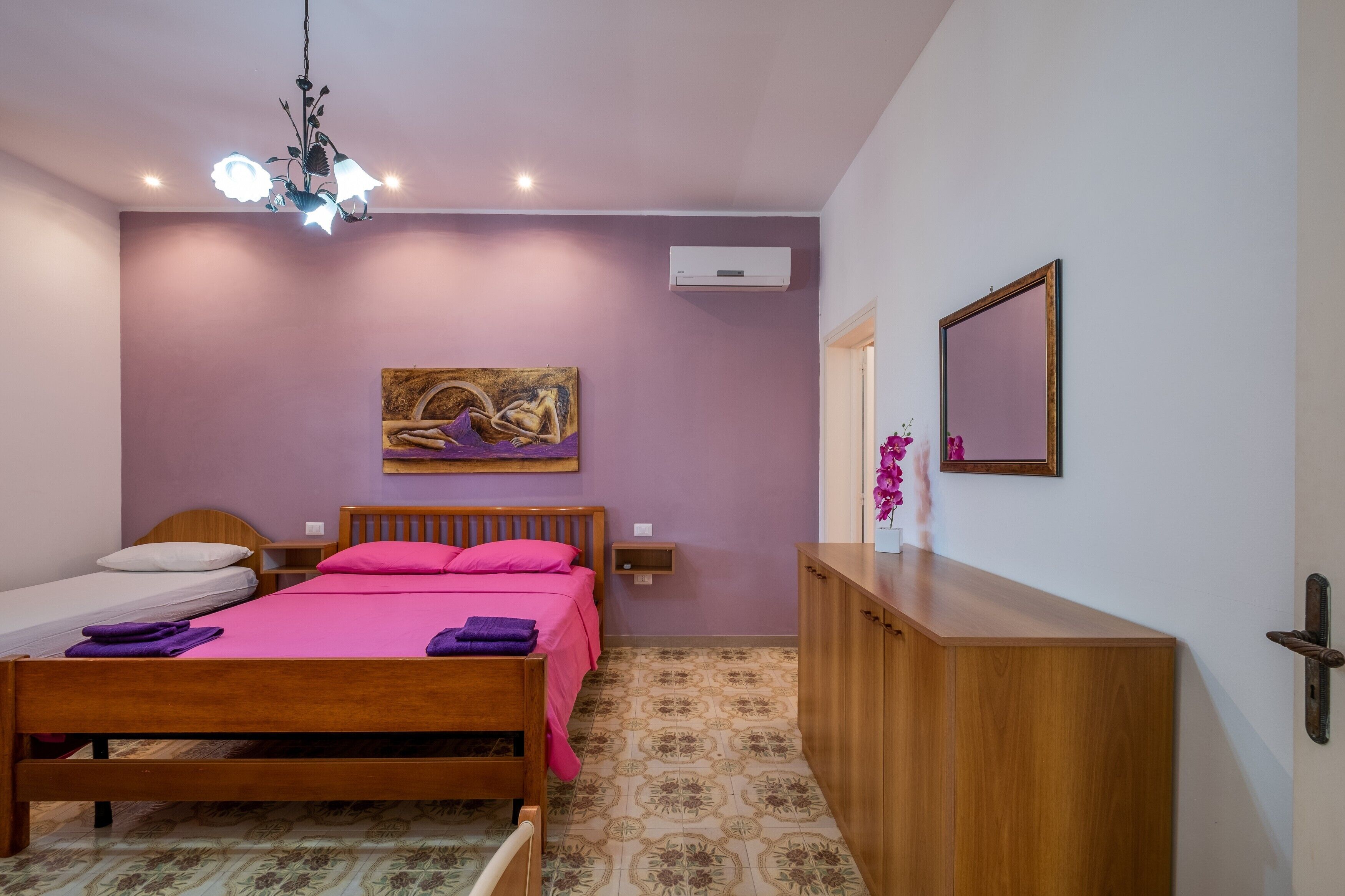 Une chambre à coucher avec un lit en bois, une table de chevet, une commode, un tableau au mur et un luminaire au plafond.