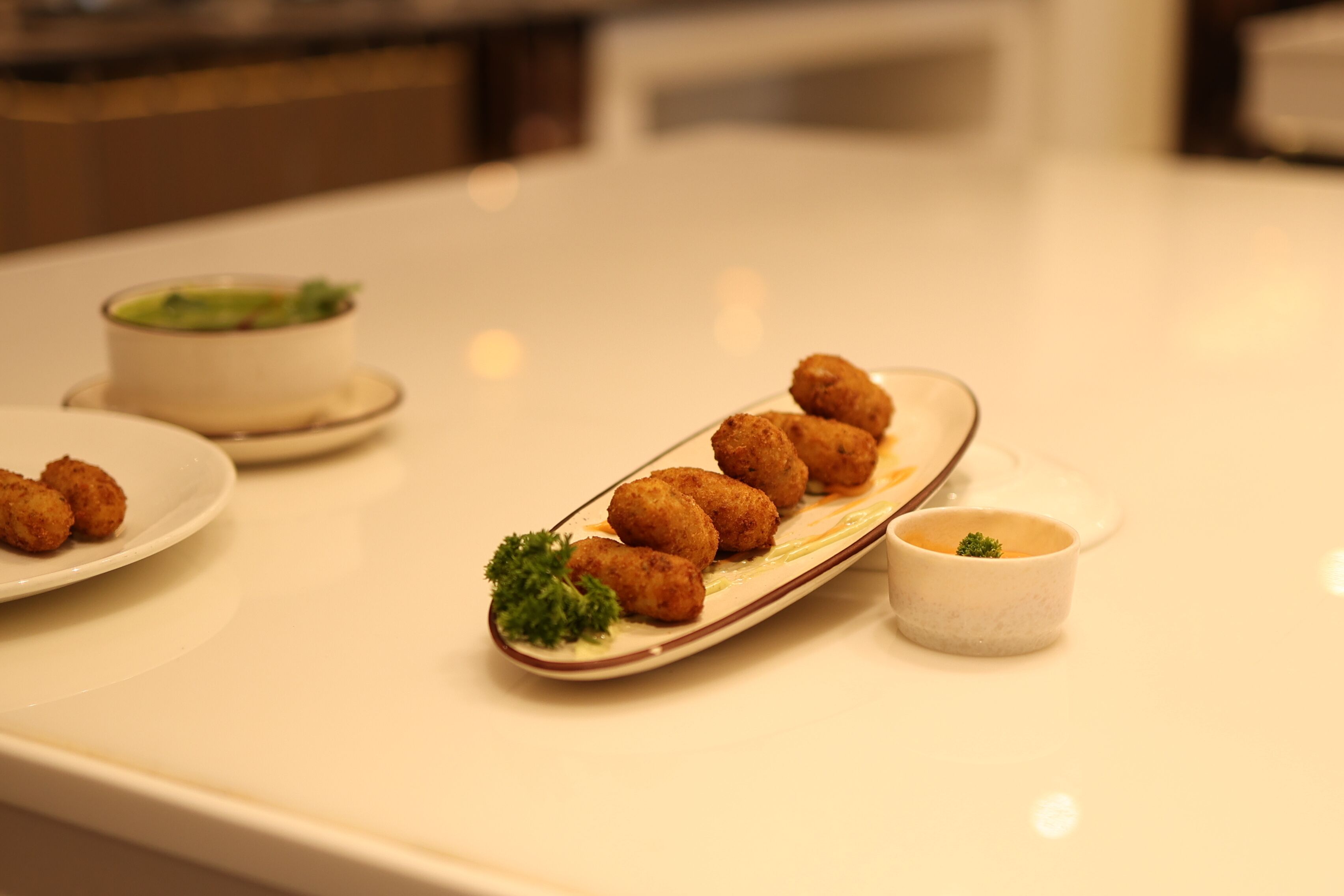 Een tafel met een bord kroketten, een kleine schaal saus en een kom soep.