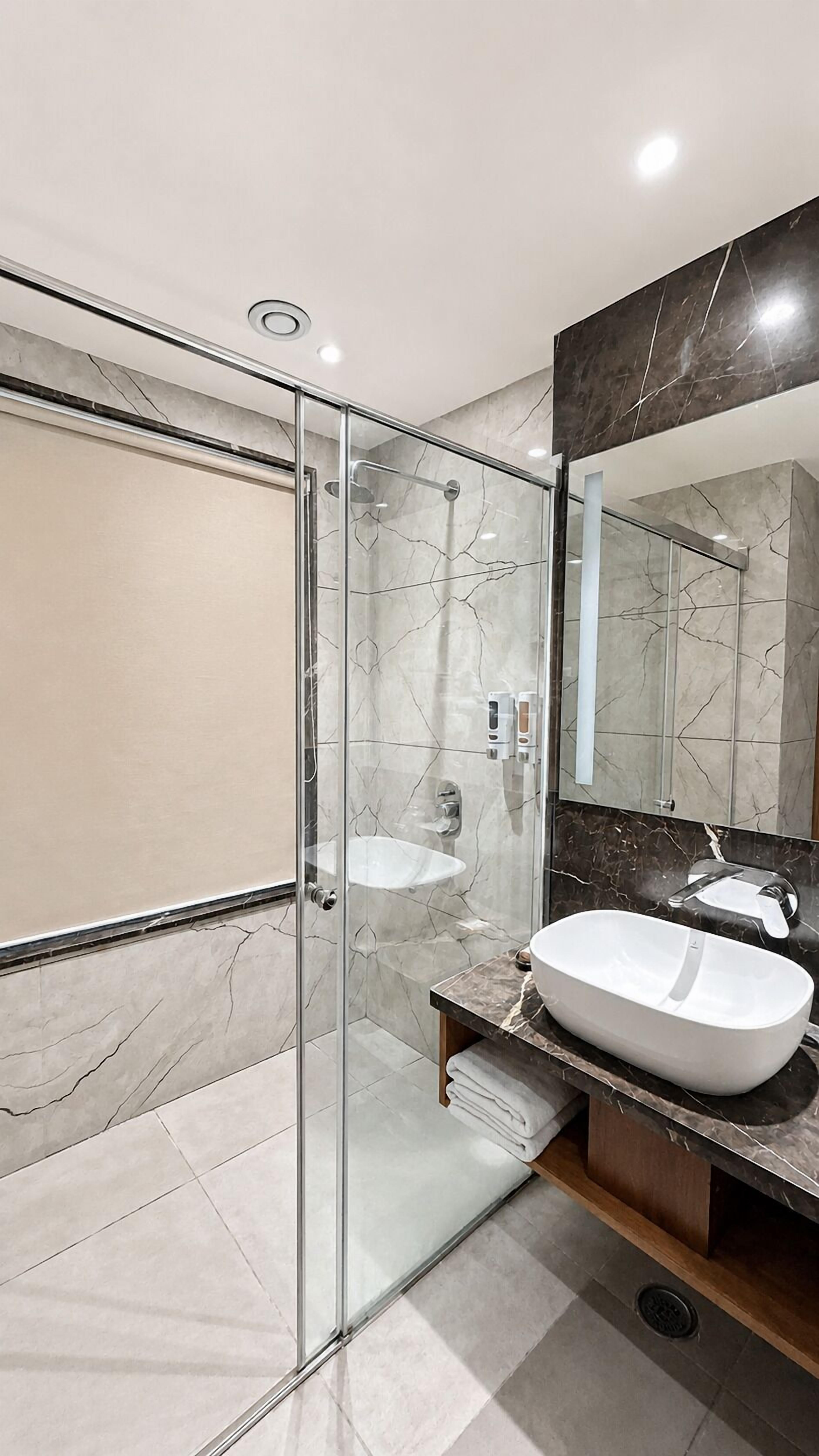 A modern bathroom with a glass-enclosed shower, a white sink, and a large mirror.