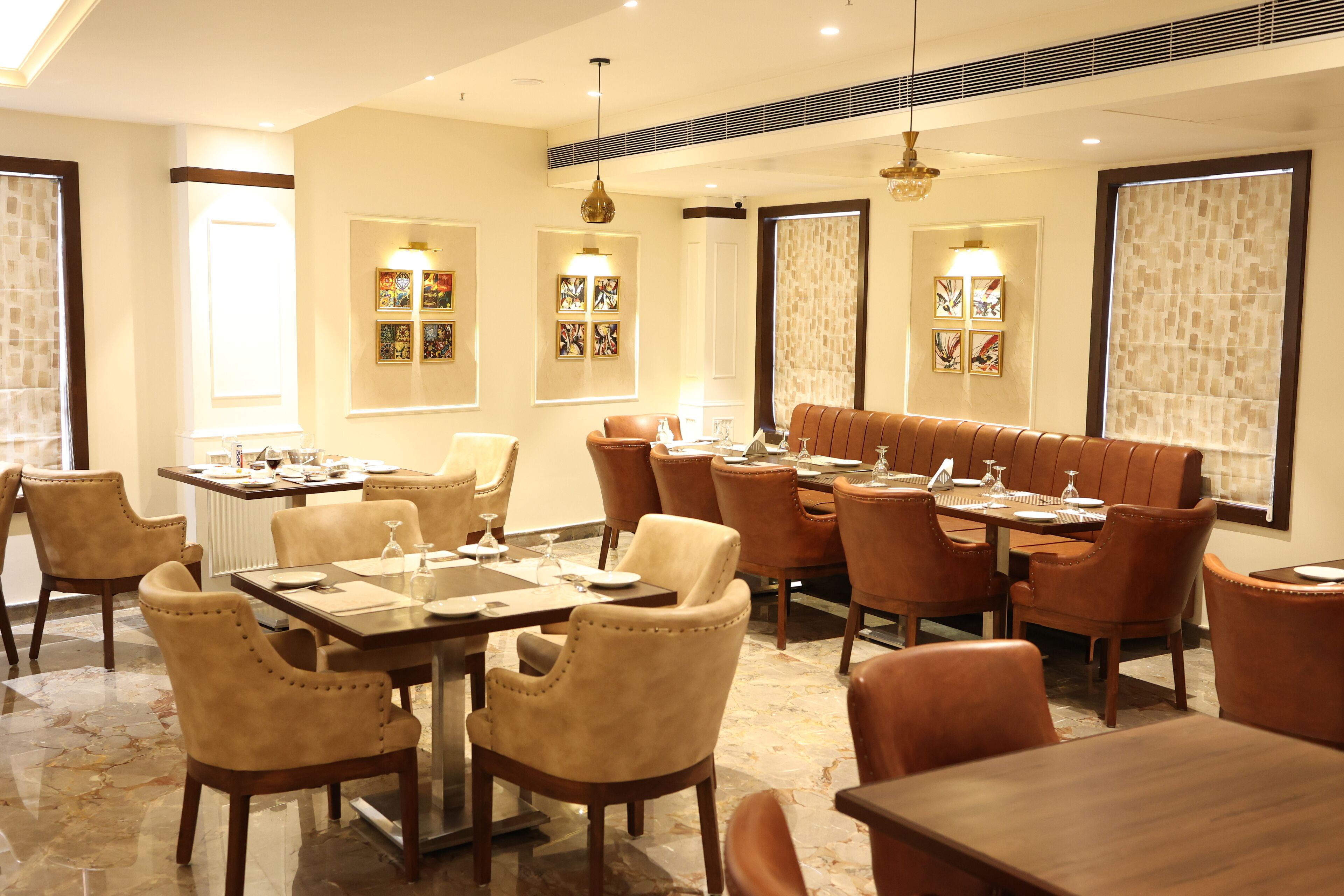 A dining area with multiple tables and chairs, well-lit by pendant lights, and decorated with framed artwork on the walls.