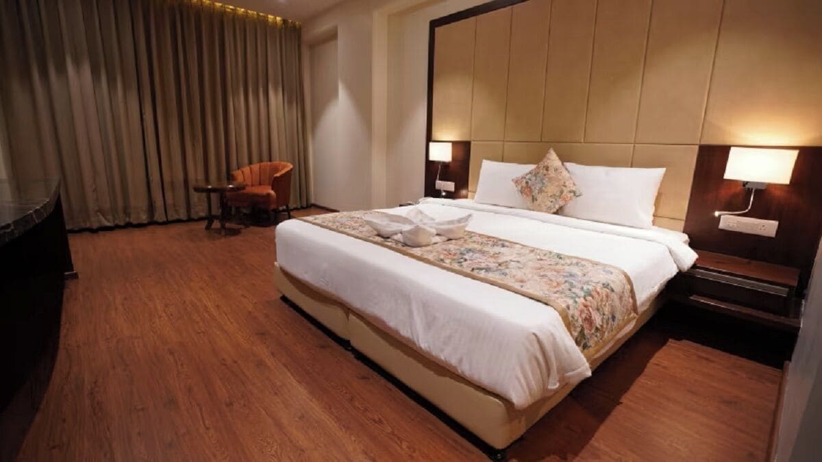 Ein Hotelzimmer mit einem großen Bett, einem Sessel, einem Schreibtisch und einem Vorhang.