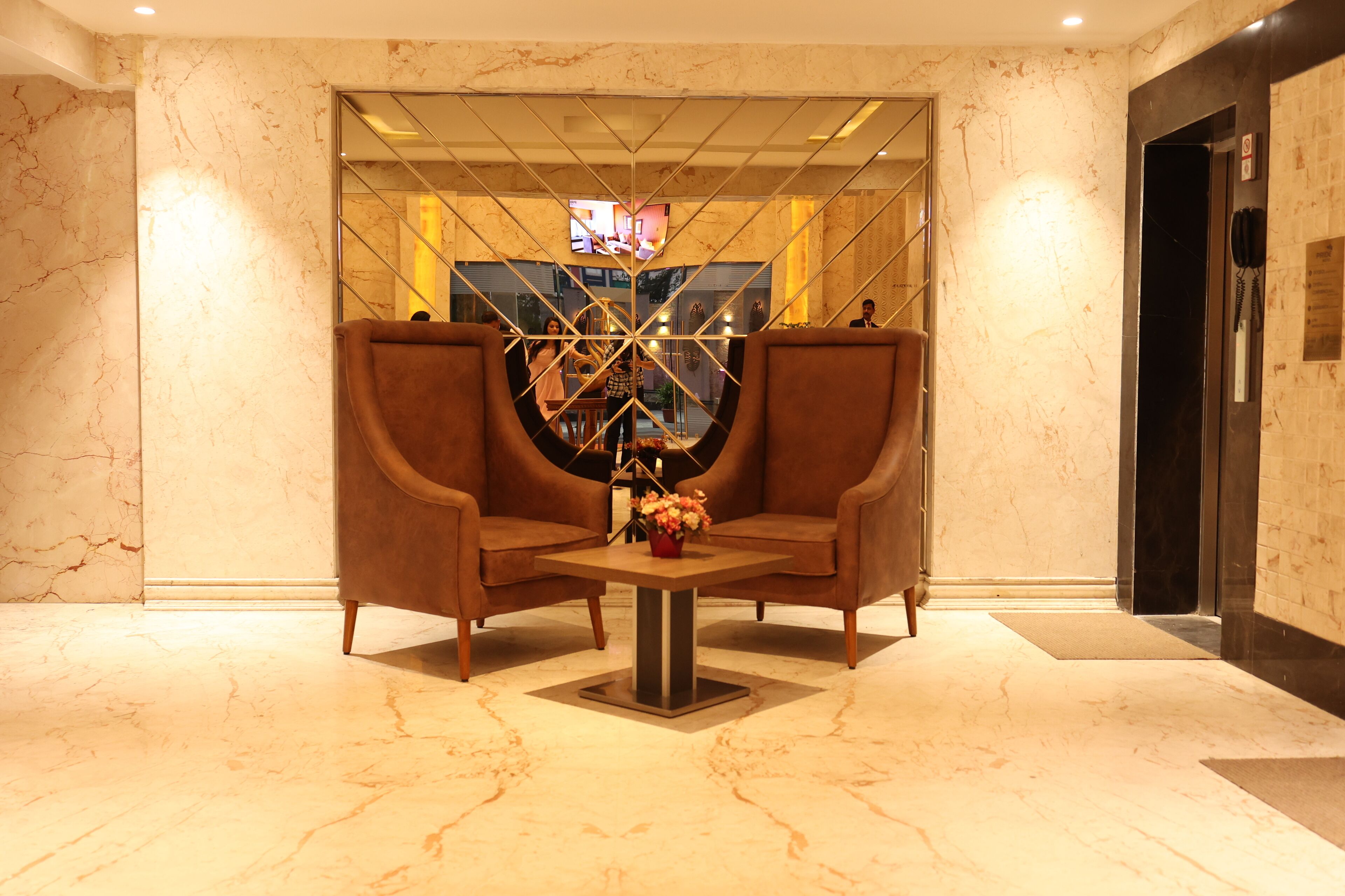 A lobby with two brown armchairs, a central table with a vase of flowers, and a large mirror reflecting the interior.