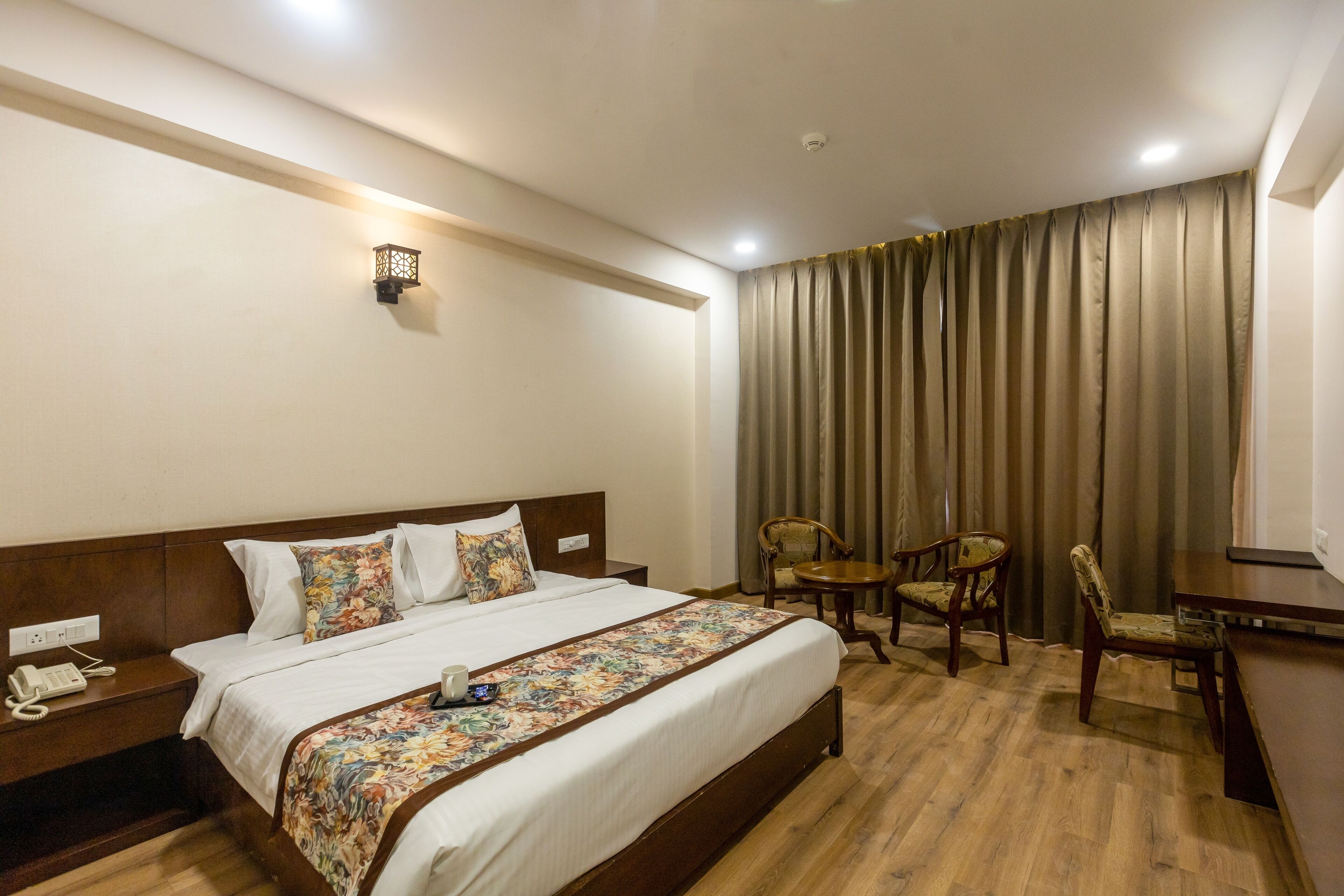 A hotel room with a large bed, a bedside telephone, a small table with chairs, and a curtain.