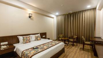 A hotel room with a large bed, a bedside telephone, a small table with chairs, and a curtain.
