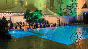 Ein Hotelpoolbereich mit großem Pool, überdachten Sitzgelegenheiten und einem mehrstöckigen Gebäude mit Fenstern.