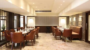 A spacious dining area with marble flooring, wooden tables and chairs, and a central seating area with a cushioned bench.
